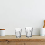 Two clear glass tumblers on a wooden surface with a white background