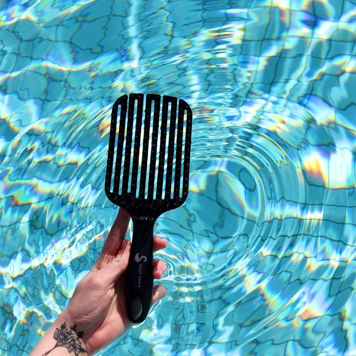 Black scream free wet brush held over a pool with blue water