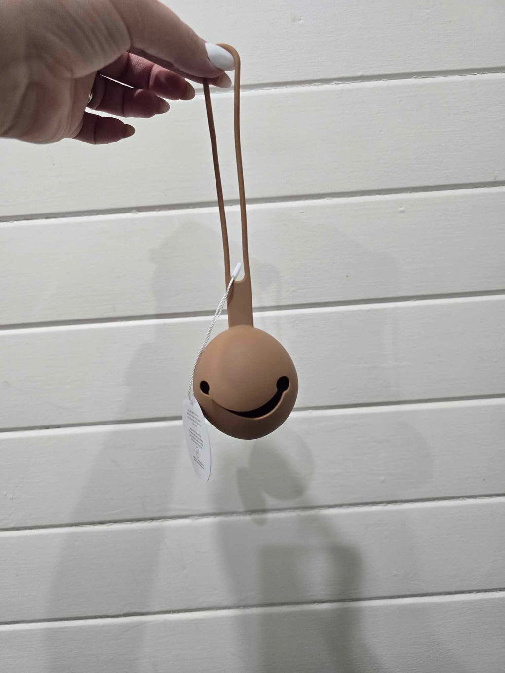 Smiley face dummy holder held by a hand against a light wooden panel background