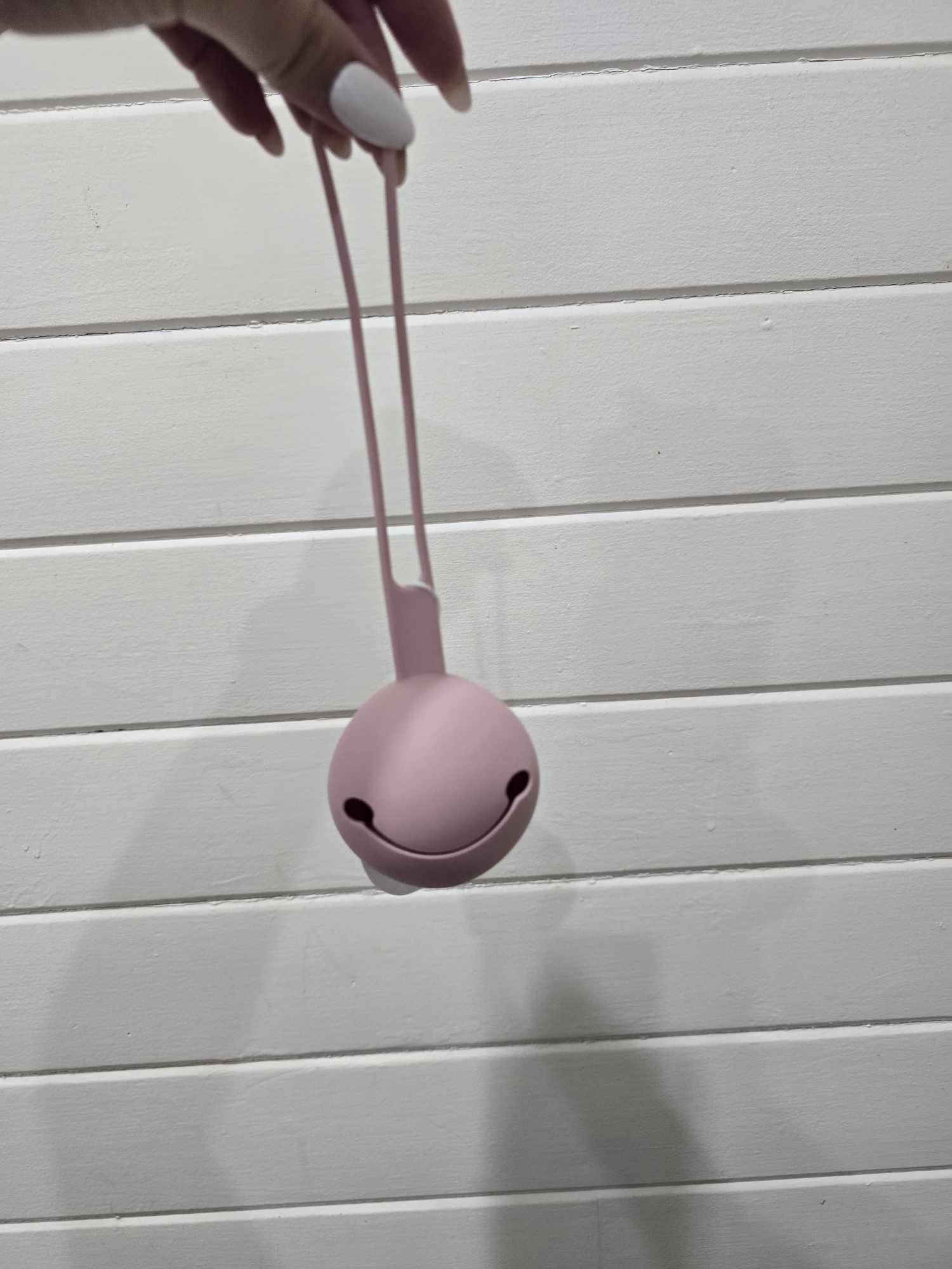 Pink dummy holder with a string held by a hand on a light wooden surface