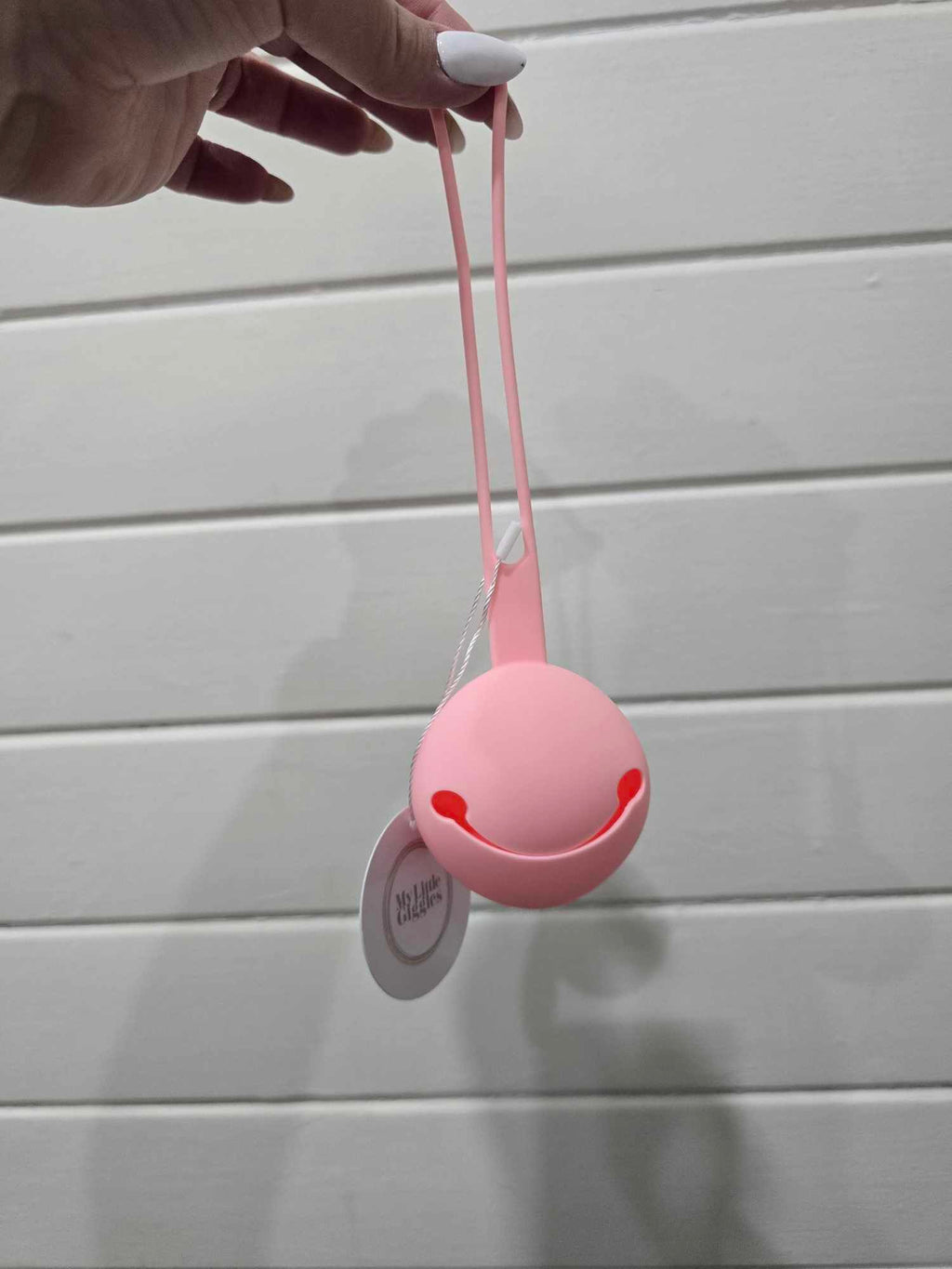 Pink dummy holder with a string held by a hand against a light gray background