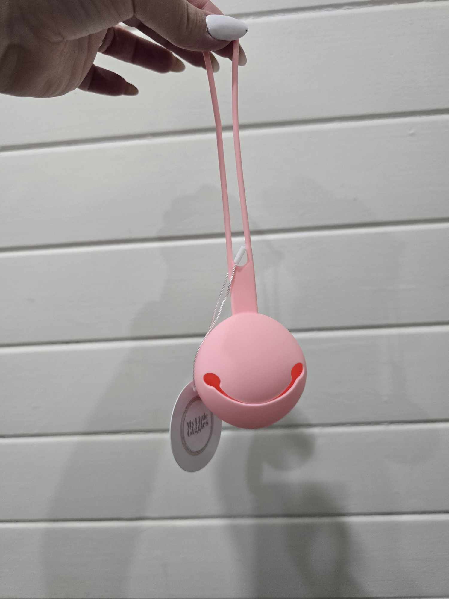 Pink dummy holder with a string held by a hand against a light gray background