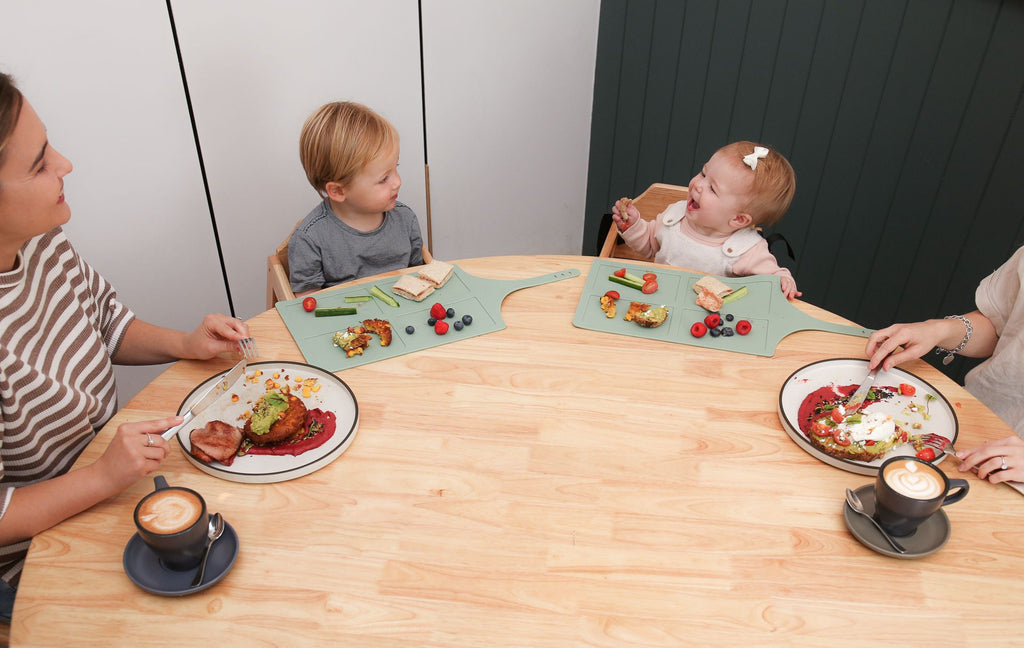 Family of four sitting around a table with plates of food and children using placemats.