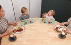 Family of four sitting around a table with plates of food and children using placemats.