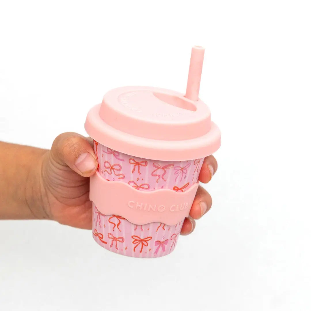 Hand holding a pink cup with a lid and straw on a white background