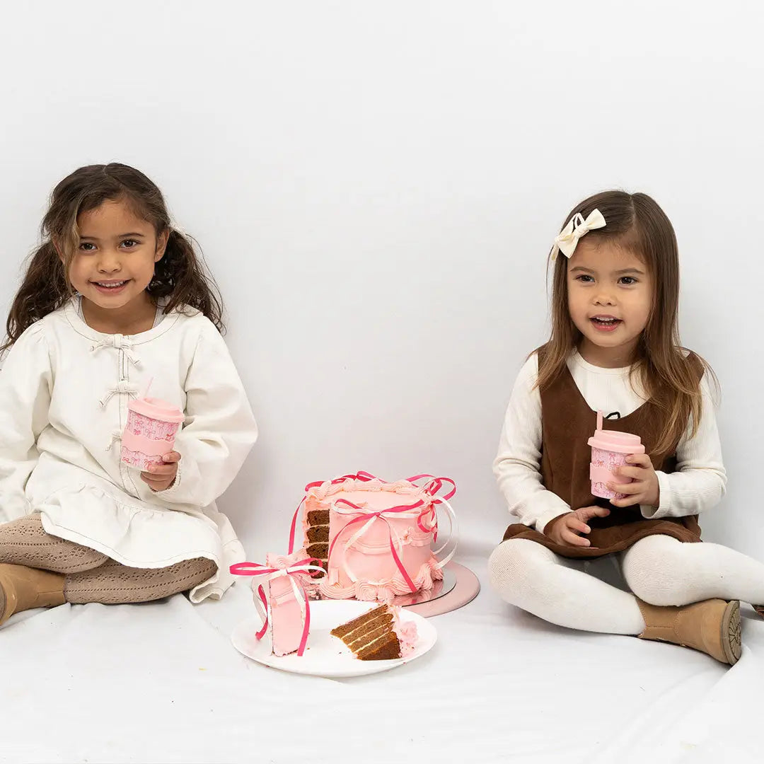Two young girls with pink drinks and a cake on a white background