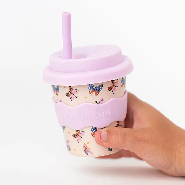 Hand holding a cup with a pink lid and straw, featuring butterfly design on a white background