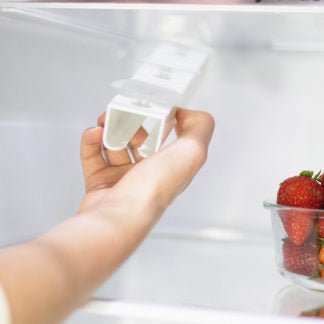 Hand holding a white food pouch and breast milk organiser with strawberries in the background