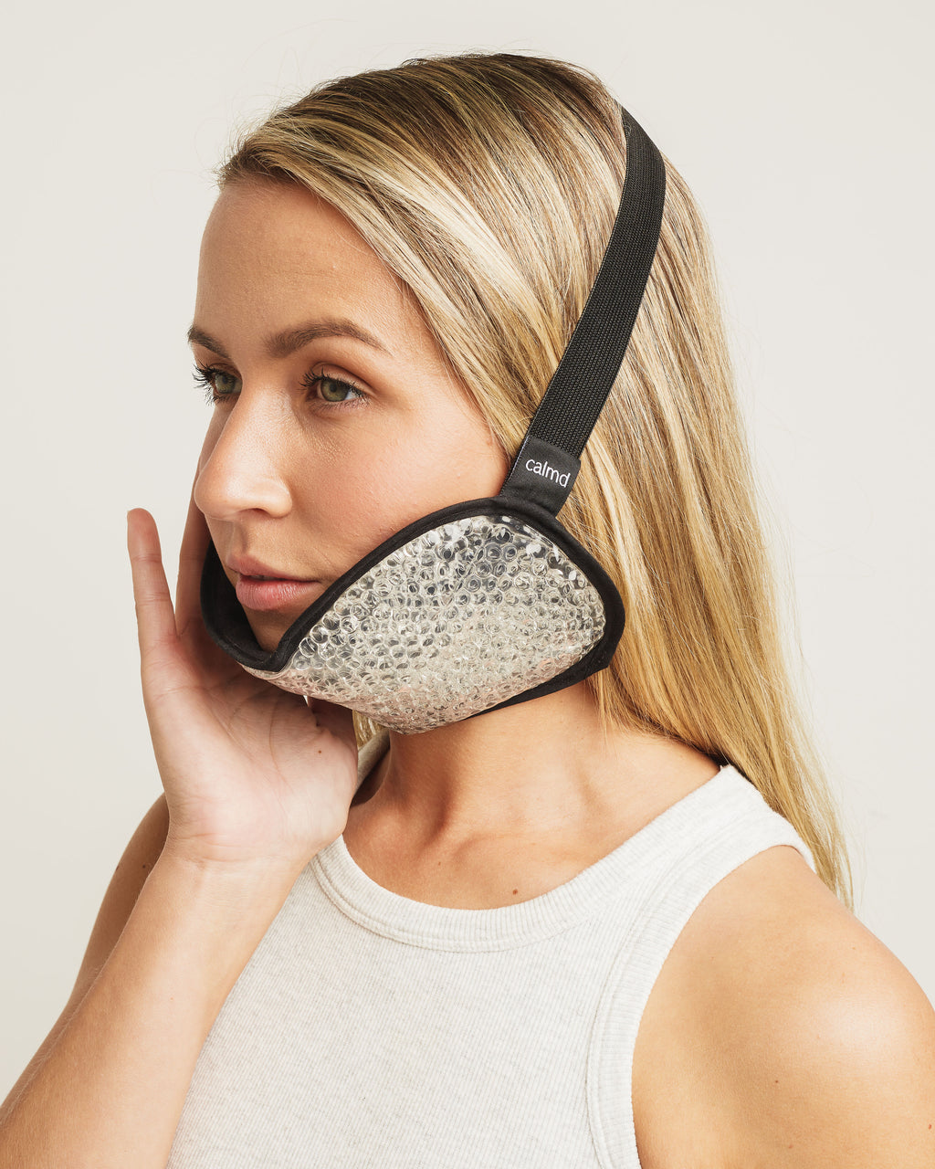 Woman wearing a black and silver eye mask with 'calm' branding on a plain background