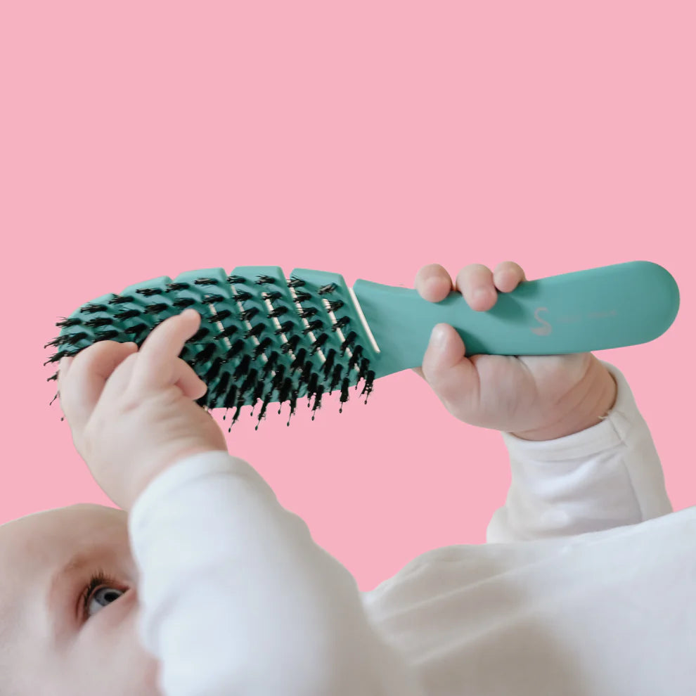 Baby holding a green hairbrush against a pink background