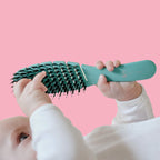 Baby holding a green hairbrush against a pink background