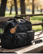 Black duffel bag with a dummy holder on a wooden bench outdoors.
