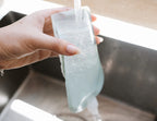 Hand holding a clear plastic bag with water being poured into it over a sink.