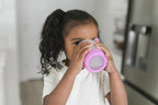 Child drinking from a pink hangable kids cup in a kitchen setting