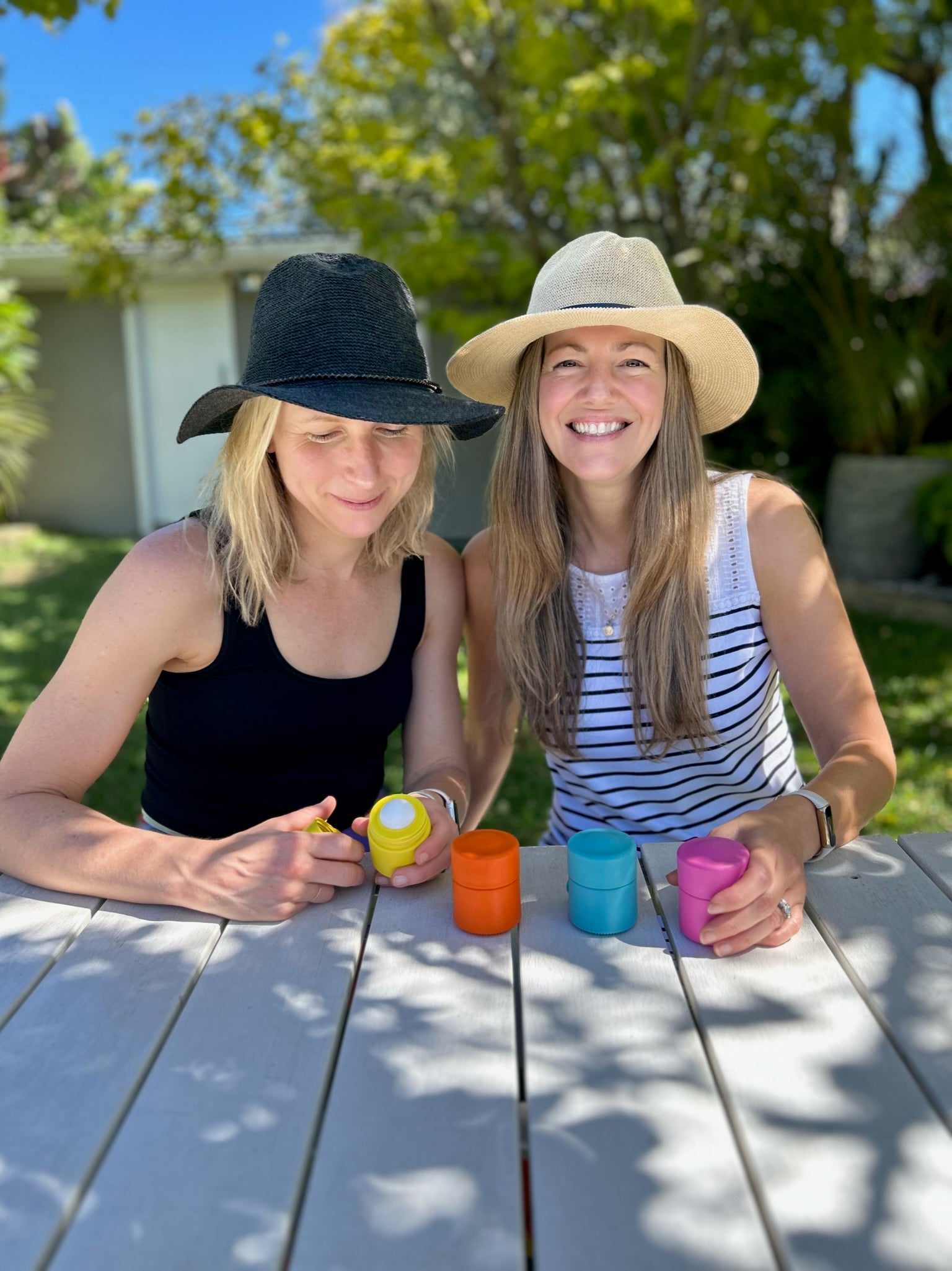 Two women sitting at a table outdoors with Solmates Refillable Sunscreen Applicator