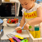Child in a kitchen wearing a colorful apron, cutting strawberries with toy knives.