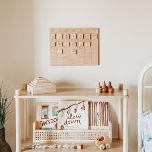 Nursery room with a wooden changing table, toys, and decorative items on a light beige wall.