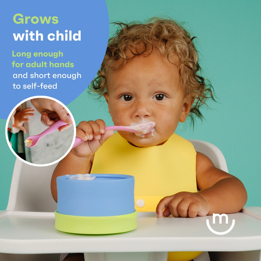 Child using a pink spoon with text about its suitability for growth, sitting at a table with a blue and green bowl.