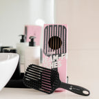 Black paddle brush on a bathroom counter with a pink box labeled 'Scream Free' in the background.