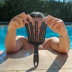 Person holding a black wet brush in front of their face by a pool
