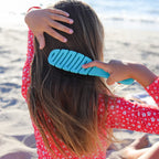 Person combing their hair with a blue comb on a beach.