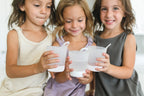 Three children holding white hangable kids cups and smiling.