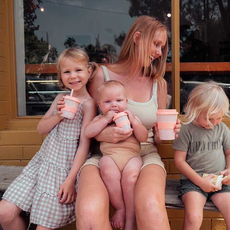 Woman with three children sitting on a bench, all holding pink cups.
