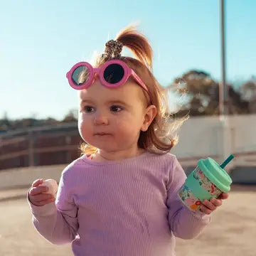 Child wearing pink sunglasses and holding a colorful cup outdoors