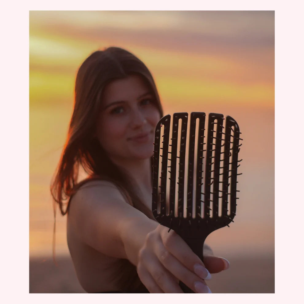 Woman holding a scream free hairbrush with a sunset background