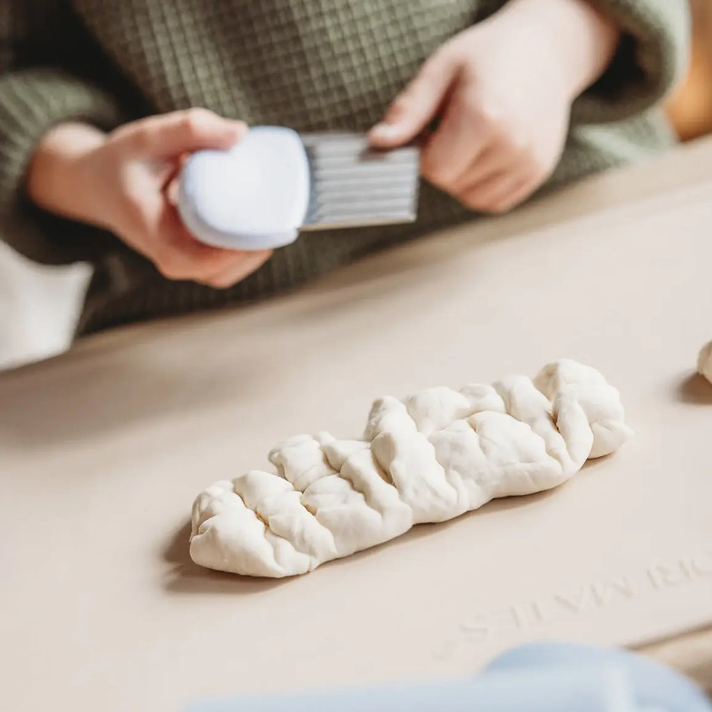 Person brushing a braided piece of dough with a brush on a wooden surface