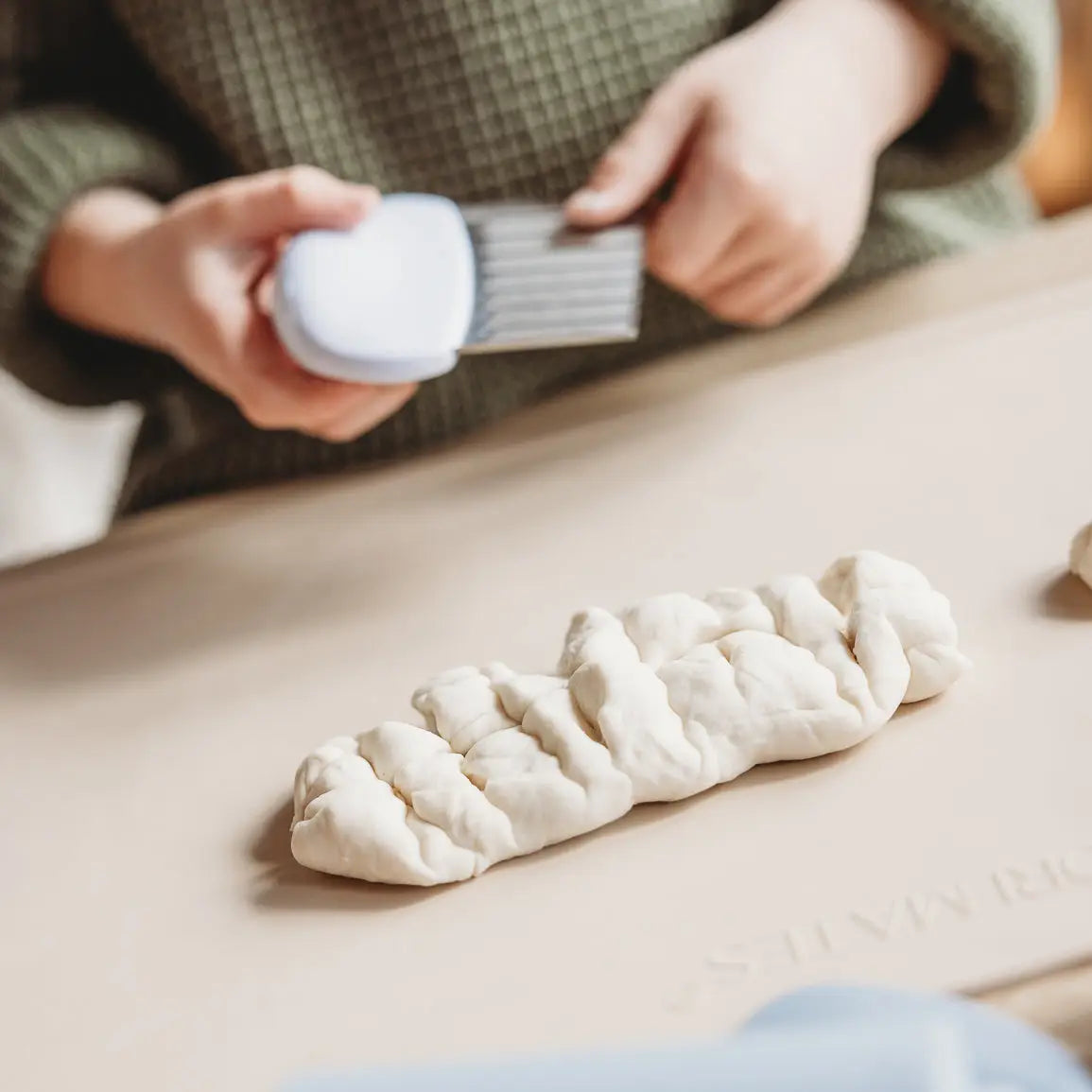 Person brushing a braided piece of dough with a brush on a wooden surface