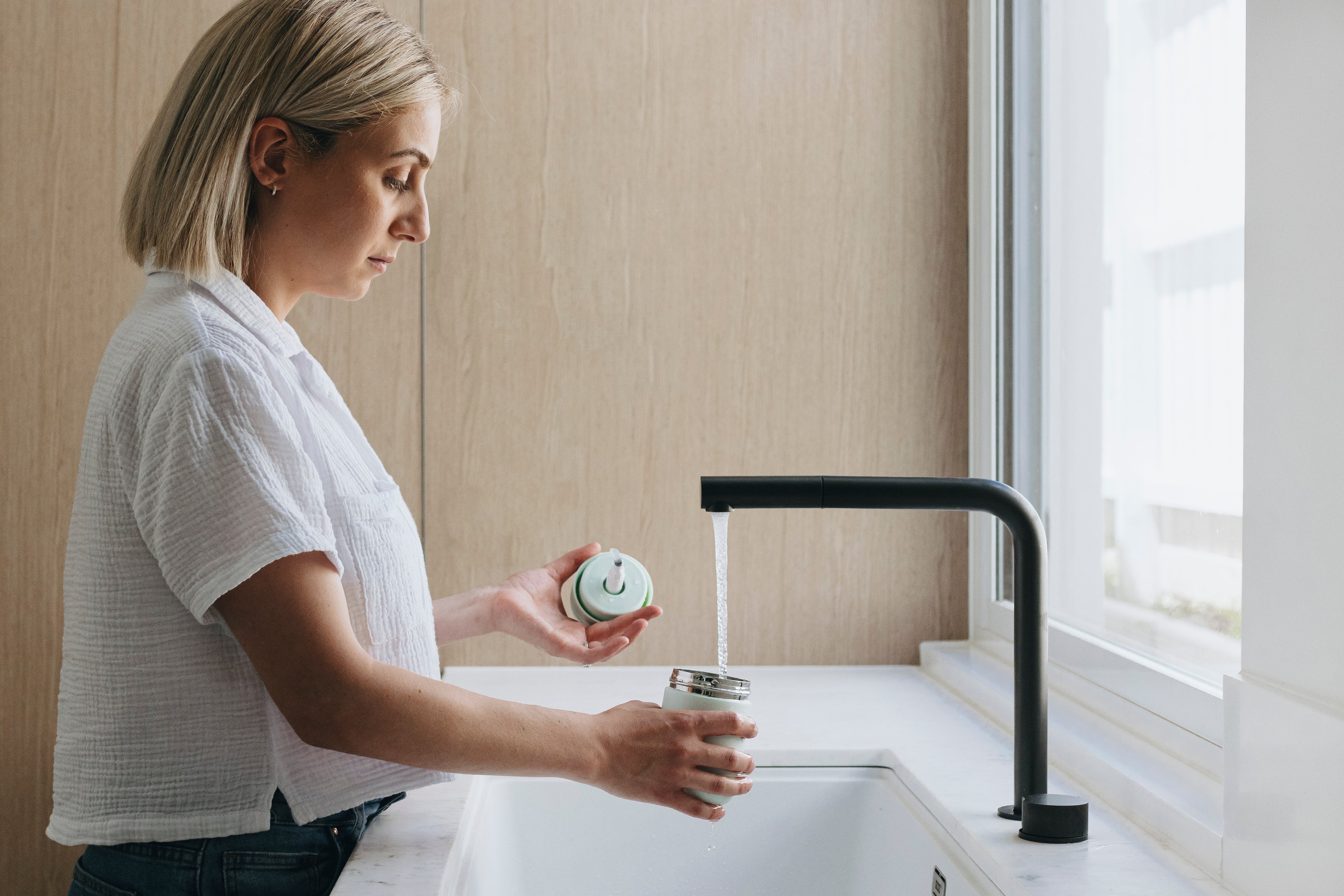 Woman using a black faucet in a kitchen to fill a warm wipes dispenser 