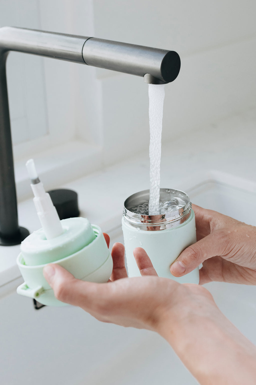 Person filling warm water dispenser with water from a kitchen faucet.