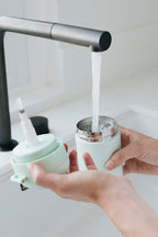 Person filling warm water dispenser with water from a kitchen faucet.