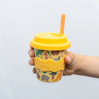 Yellow cup with animal pattern and straw held by a hand against a light gray background