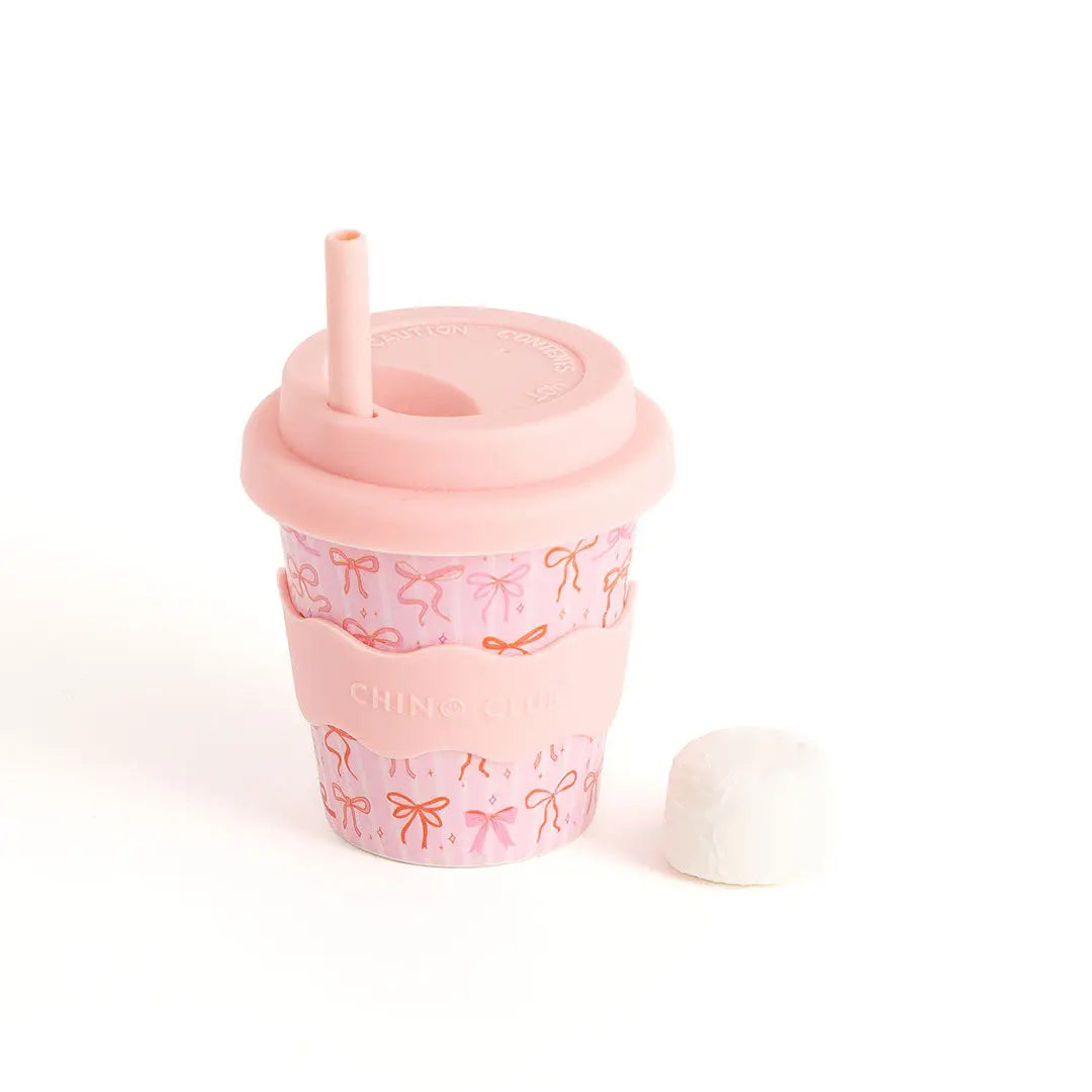 Pink tumbler with bow pattern and straw on a white background