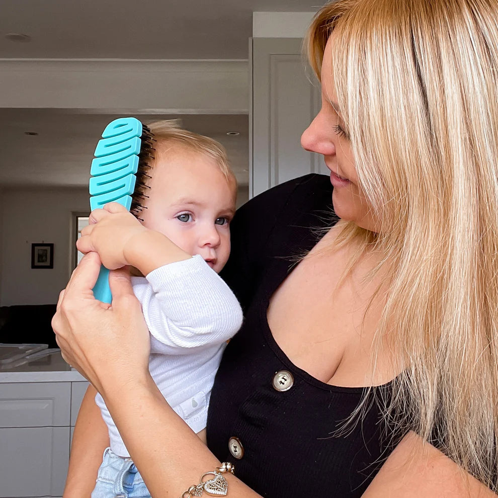 Woman holding a child with a blue hairbrush in a home setting